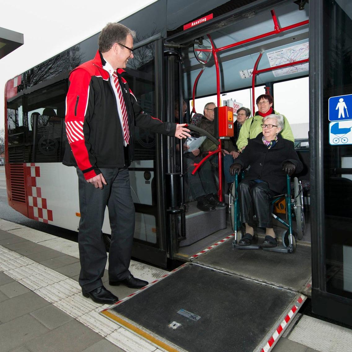 Busfahrer klappt Rollstuhlrampe für Frau im Rollstuhl aus