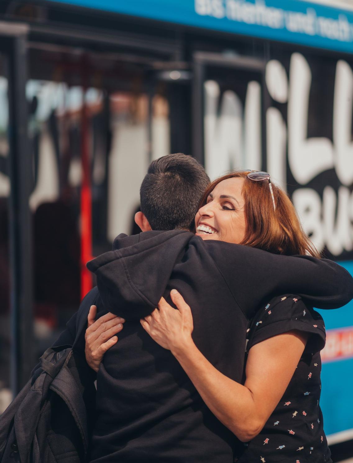 Mutter umarmt ihr Kind vor dem Bus der VOS