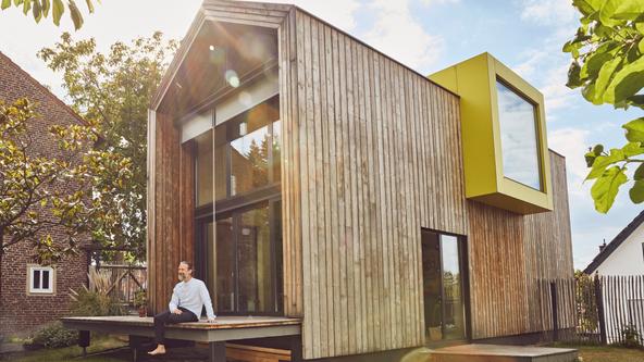 Mann sitzt auf seiner Terrasse vor seinem nachhaltigen Holzhaus