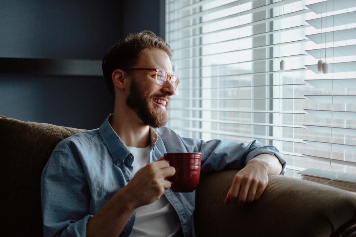 Mann mit Kaffeetasse in der Hand schaut aus dem Fenster